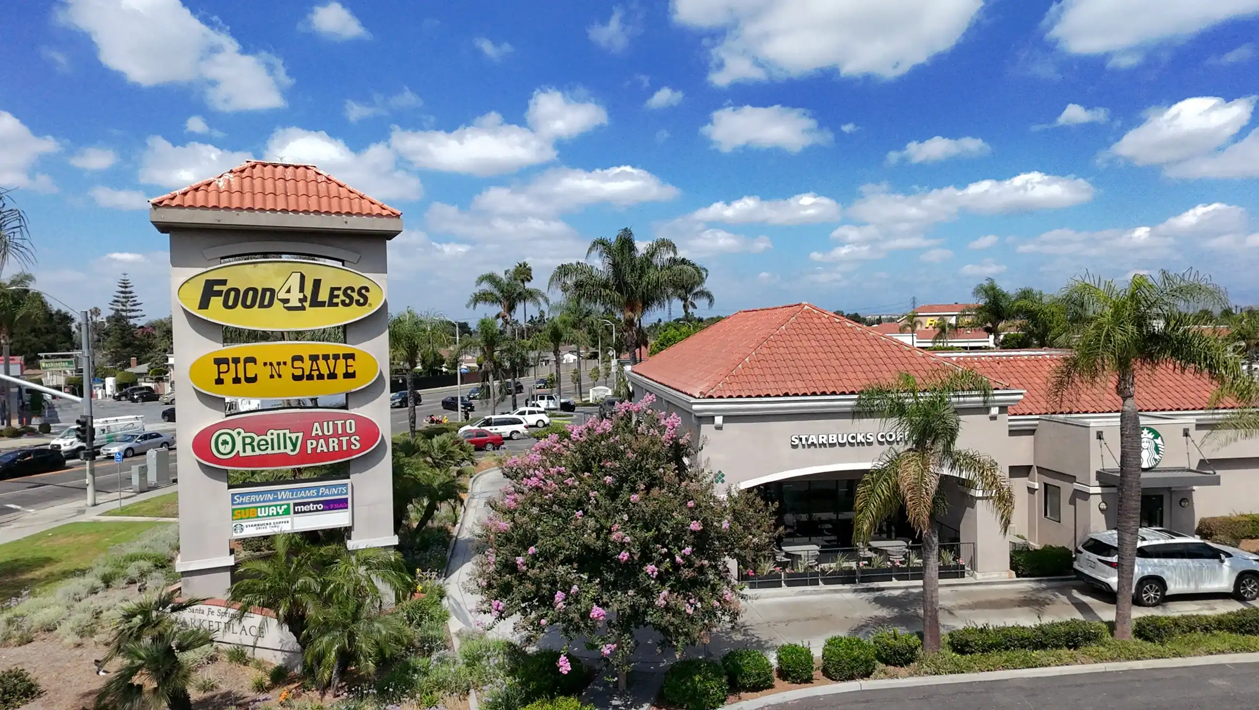 Food 4 Less and Starbucks storefronts at Santa Fe Springs Marketplace, showcasing prominent signage and landscaping, highlighting the center's diverse retail offerings and high visibility.
