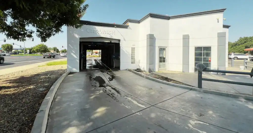 Sassy Carwash drive-through facility in Hanford, California, featuring a modern white and gray exterior, located on a busy street corner with cars and traffic lights in the background.