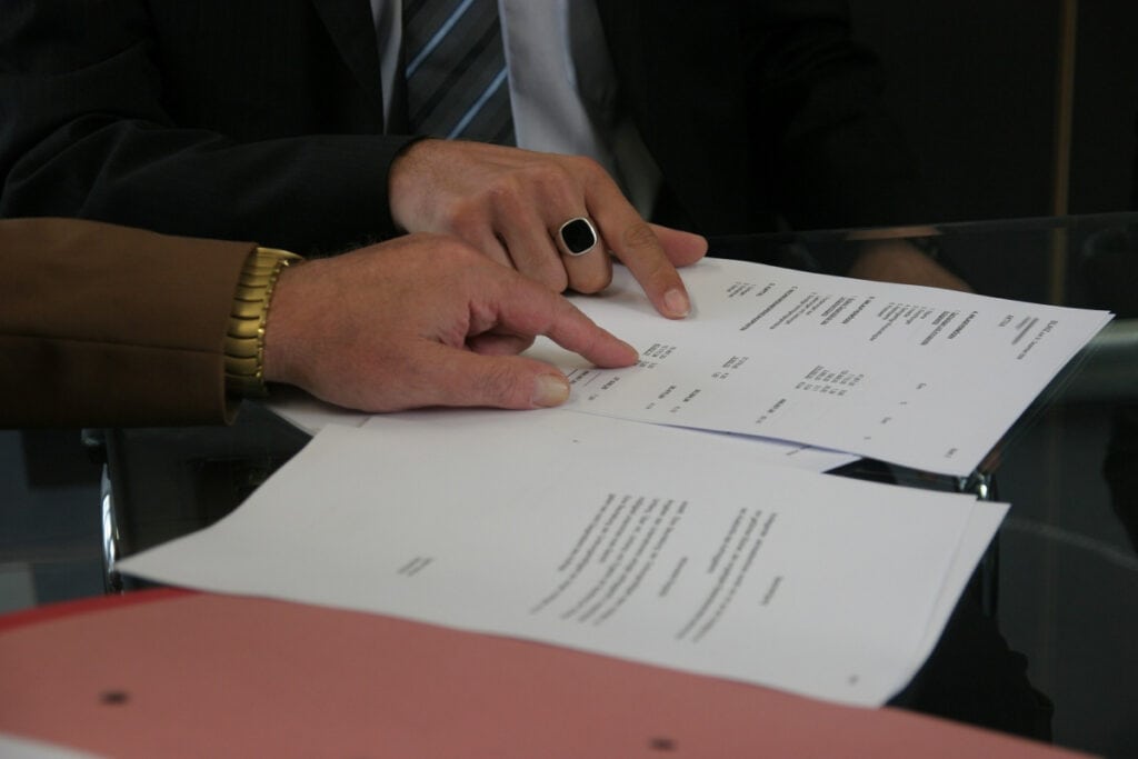 Two professionals pointing at documents on a table while reviewing property or financial paperwork during a brokerage consultation.