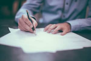 Person reviewing and signing commercial lease documents at a desk, close-up of hands holding a pen.