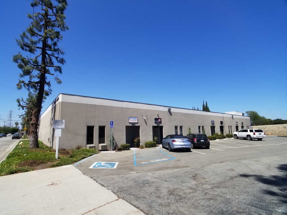 Exterior view of a single story commercial office building with parking spaces, cars, and a blue sky.
