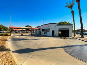 A sunny outdoor view of a drive through car wash with vacuum stations and shaded canopies at a clean, open concrete lot.